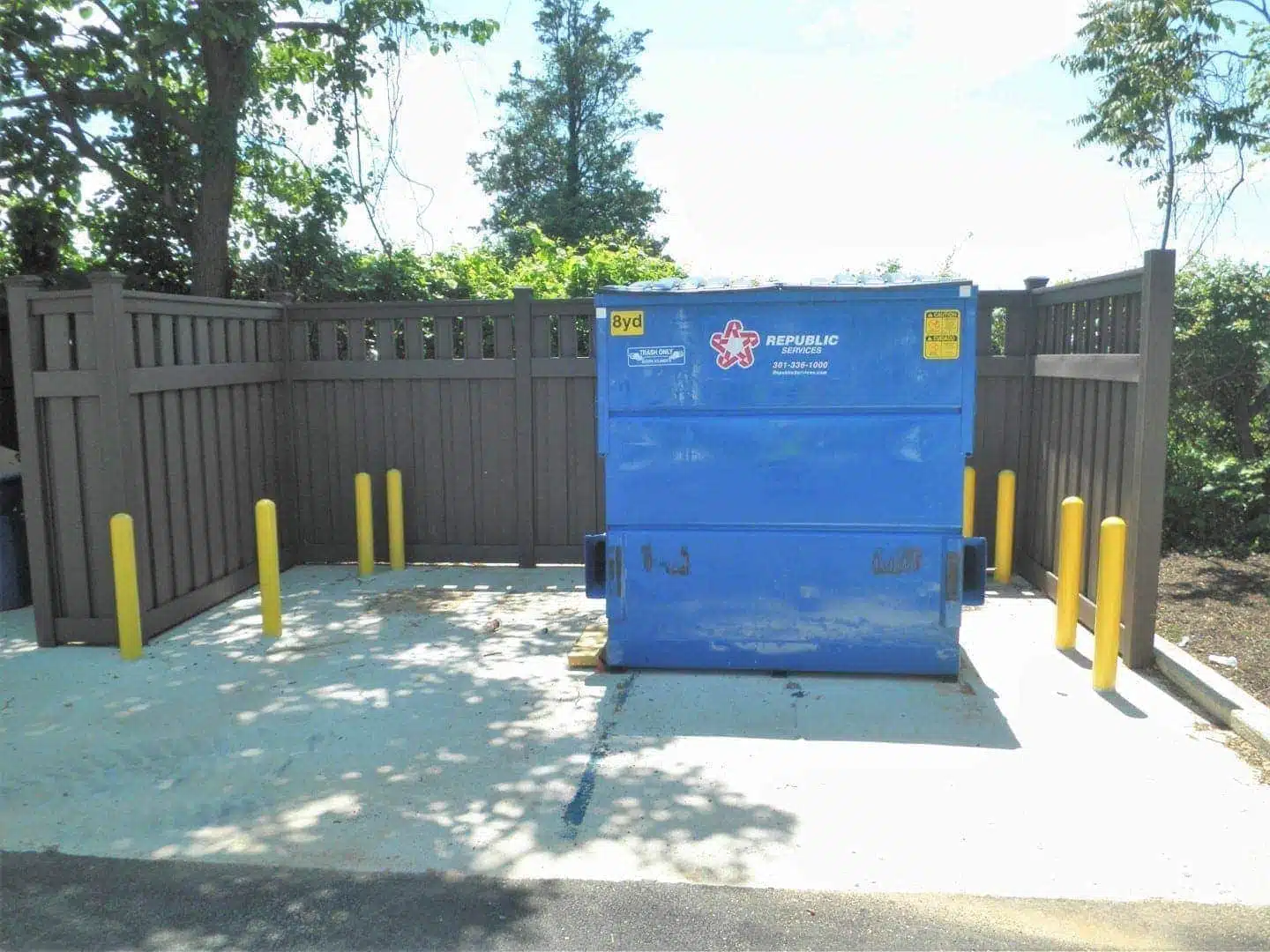 A dumpster in a trash enclosure made from Trex Fencing