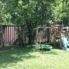 A shady backyard in Florida with a playset and a Trex privacy fence in the background